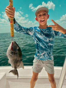 kid fishing near shore holding a triggerfish